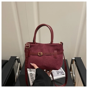 Détail du cabas en daim bordeaux avec poignées en cuir et boucles métalliques dorées