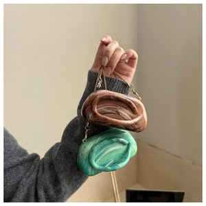 Detail of marble pattern acrylic clutch with gold chain strap in brown and green colors