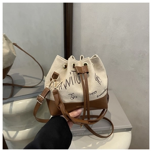 Detail of canvas bucket bag with leather base, drawstring closure, and artistic graffiti