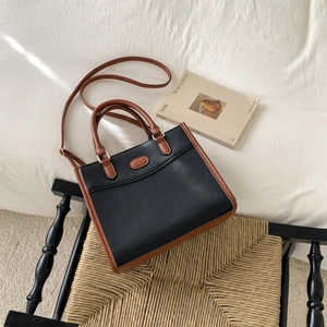 Vintage black and brown leather tote bag with top handles on a wooden chair