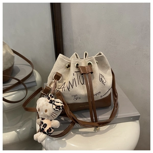 Close-up of canvas bucket bag with leather base and a cute plush kitty charm