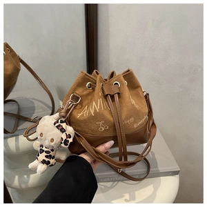 Detail of a brown drawstring bucket bag with a plush bear charm and cherry pattern