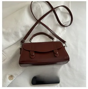 Detail of a brown leather small square bag shown next to a smartphone for size comparison