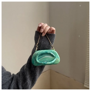 Κοντινή λήψη πράσινης μαρμάρινης τσάντας clutch με καλλιτεχνικό ανάγλυφο και χρυσή αλυσίδα