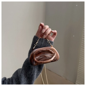 Detail of acrylic clutch bag with brown marble texture and thin gold chain strap