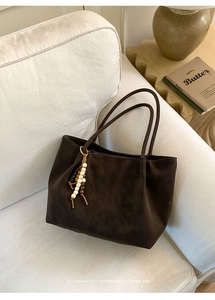 Detail of a large brown suede tote bag with beaded tassel on a soft fabric sofa