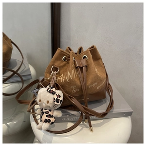 Detail of brown bucket bag with plush charm on a white stool in a minimal setting