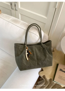 Detail of olive green suede tote bag featuring retro wooden bead charm on a sofa