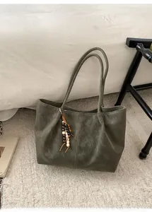 Detail of dark olive green tote bag with wooden bead tassel on cream textured rug