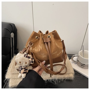 Close-up of brown bucket bag with plush cat charm on beige knit background
