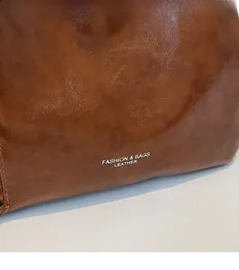 Close-up of brown textured leather crossbody bag with white fashion letter branding
