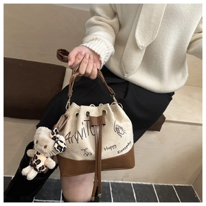 Detail of canvas bucket bag with brown leather trim and cute teddy bear charm