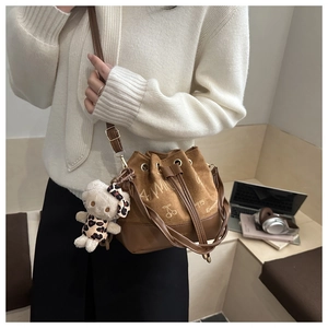 Brown suede bucket bag with cherry print and bear charm shown on a model