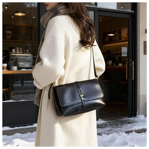 Sac bandoulière noir classique à boucle dorée porté sur un manteau blanc en hiver