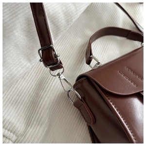 Detail of dark brown leather crossbody bag with silver metal buckles and lobster clasps