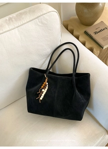 Close-up of black suede tote bag featuring unique wooden bead charms on leather handles