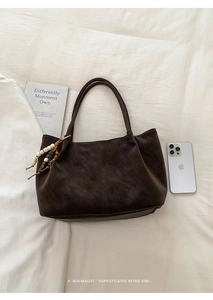 Detail view of brown suede tote bag with stylish wooden bead tassel on a soft white cloth