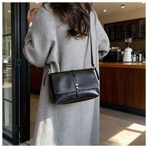 Détail d'un sac bandoulière rectangulaire en cuir noir avec boucle métallique sur l'épaule