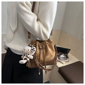 Detail of a brown suede bucket bag with white lettering and a plush cat doll charm
