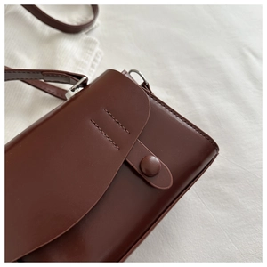 Macro detail of dark brown mini crossbody bag showing stitching and smooth PU leather texture