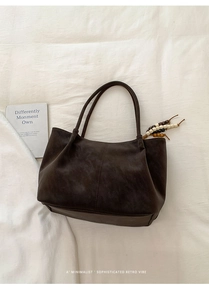 Detail view of brown matte suede tote with colorful beaded pendant and slim handles