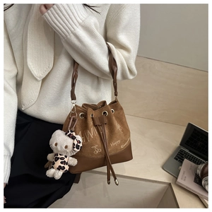 Brown suede bucket bag with graffiti print and plush cat pendant on a model's shoulder