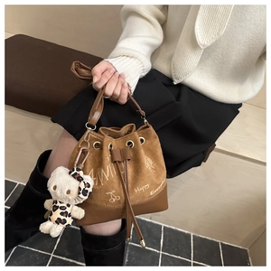 Close-up of brown suede bucket bag with cartoon prints and plush kitty charm