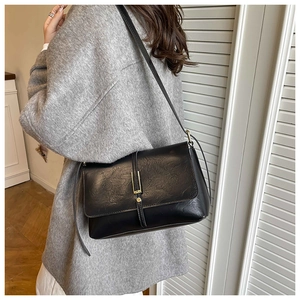 Détail d'un sac bandoulière noir vintage avec boucle dorée sur un manteau de laine gris