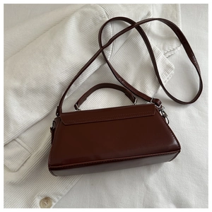 Detailed view of deep brown vintage crossbody bag with silver buckles on white corduroy