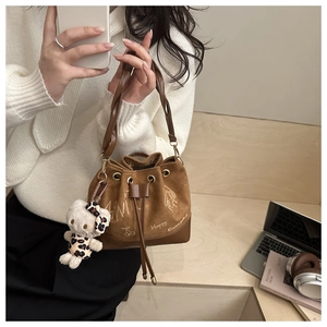 Detail of vintage brown suede bucket bag with leather strap and plush bear charm