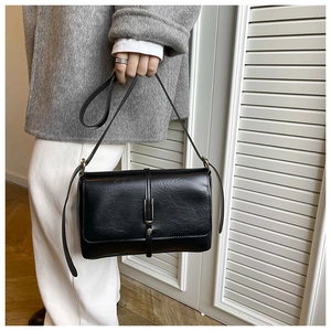 Detail van minimalistische zwarte crossbodytas met gouden gesp op een grijze jas