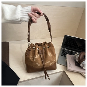 Close-up of caramel bucket bag with braided handle and Happy Everyday lettering on body