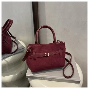 Gros plan sur un sac à main bordeaux en cuir givré avec boucle dorée et bandoulière