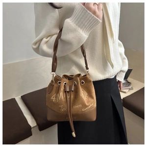 Detail of a brown suede bucket bag featuring a woven handle and artistic graffiti prints