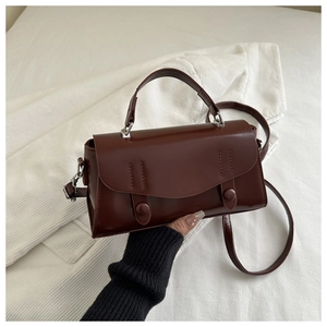 Detail view of a vintage dark brown leather crossbody bag with stitching and circular buckles