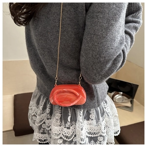 Detail of a mini acrylic marble texture bag with a fine gold chain strap in orange red
