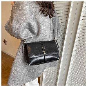 Detail van vintage zwarte leren crossbodytas met gouden gesp op een grijze jas outfit