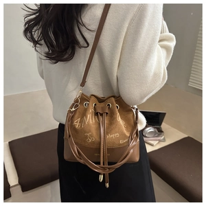 Detail view of brown suede bucket bag with hand-drawn graffiti on a white knit sweater