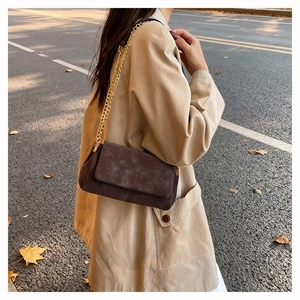 Detail of dark brown suede shoulder bag with gold chain strap in autumn street setting