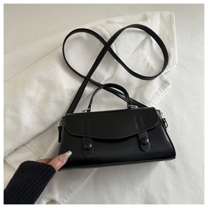 Detail view of a matte black leather square bag with double buckles on textured white fabric