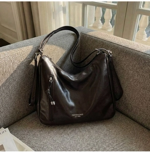 Detail of dark brown hobo bag with front vertical zipper and leather tassel on a sofa