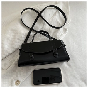 Close-up of minimalist black vintage crossbody bag with flap and dual button detail