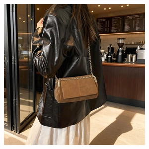 Close-up of brown suede crossbody bag with gold chain strap worn by a model in a cafe