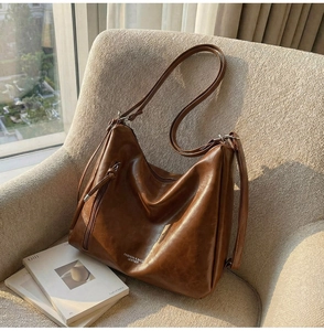 Close-up of brown leather hobo bag on a sofa showing matte texture and adjustable strap
