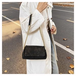 Detail of black suede chain bag with cross stitching worn with a white coat outdoors