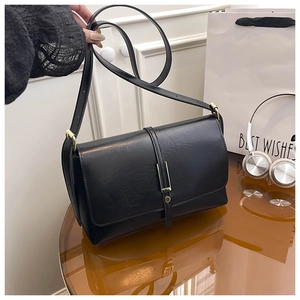 Détail du sac bandoulière en cuir mat noir avec sangle verticale et boucle dorée