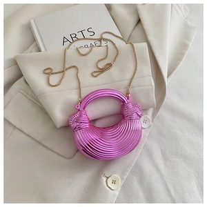 Détail du sac demi-lune fuchsia métallisé à rayures posé sur un blazer blanc
