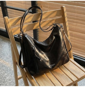 Close-up of black oil-wax leather hobo bag with zip detail on a rustic wooden chair