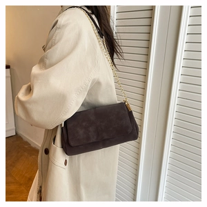 Detail of dark brown suede crossbody bag with gold chain and cross-stitch texture