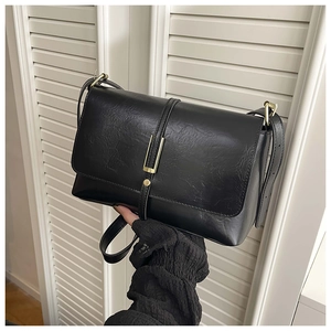 Détail d'un sac à bandoulière vintage en cuir noir avec barre métallique dorée et rivets